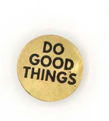 A circular brass pin with "DO GOOD THINGS" written in black.